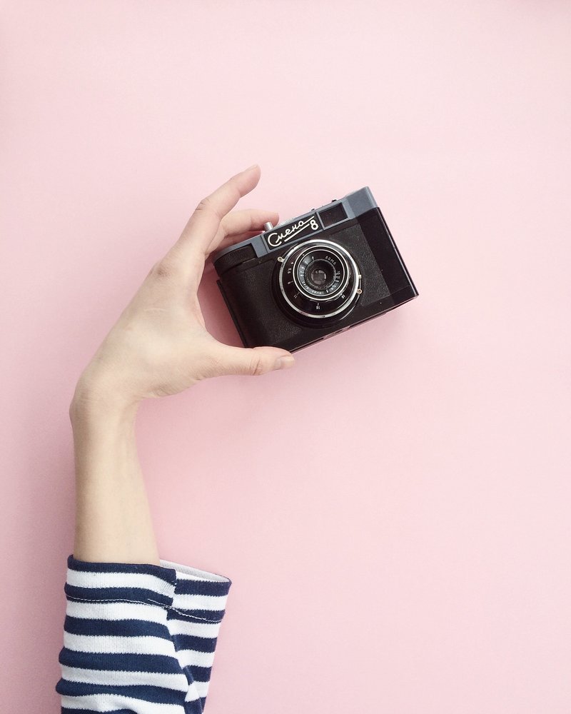 Woman holding a film camera in front of a pink backdrop.