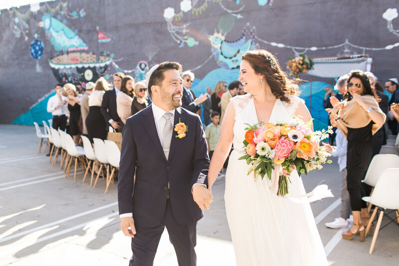 Bride and groom smile brightly at each other while holding lush bouquet after walking back down the aisle married
