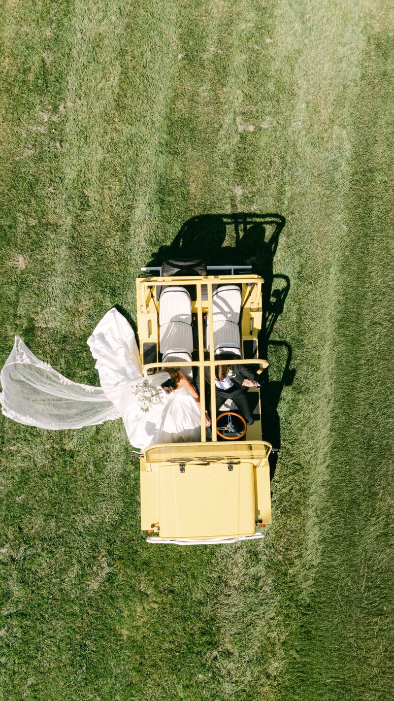 Overhead view of Anya and George in a yellow vintage Jeep on the lawn