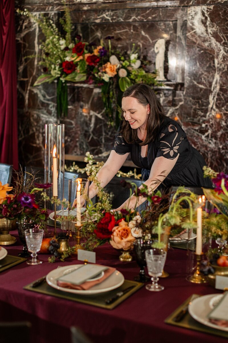 Chicago wedding planner from Savoir Fête arranging elegant table settings for a sophisticated wedding reception, showcasing meticulous attention to detail and a warm smile in a beautifully decorated venue.