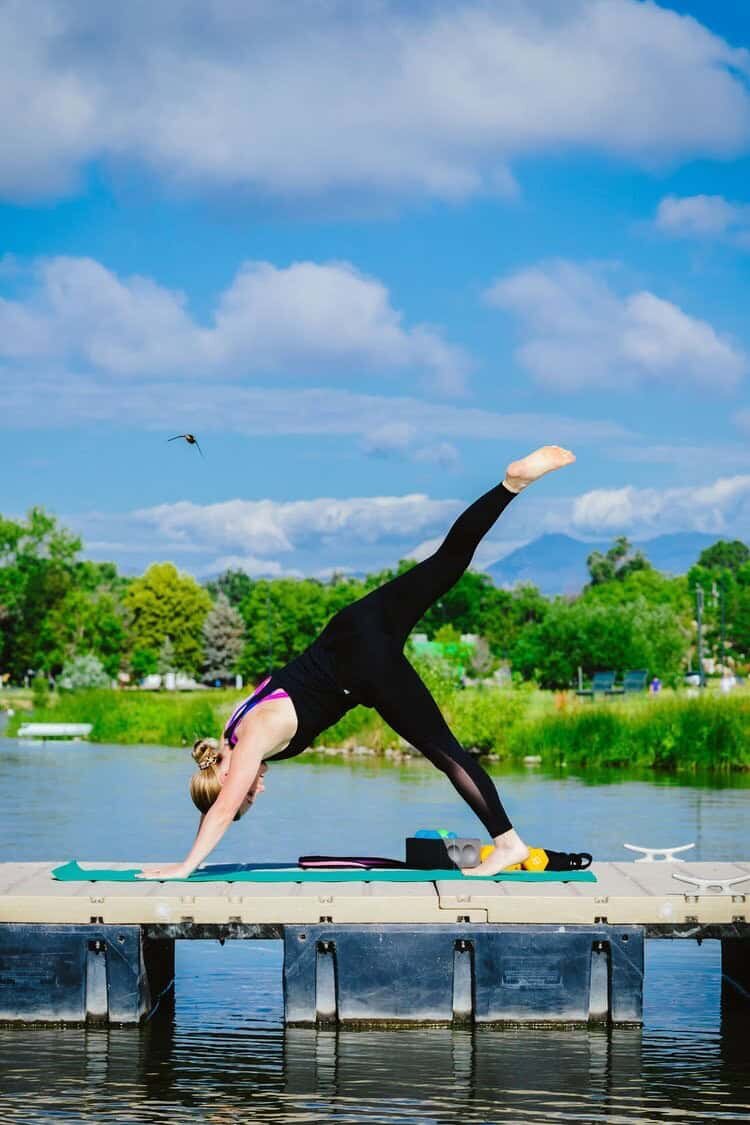 Devon Denys practicing yoga on a dock, showcasing a balance of mind and body wellness in the beautiful Colorado outdoors.