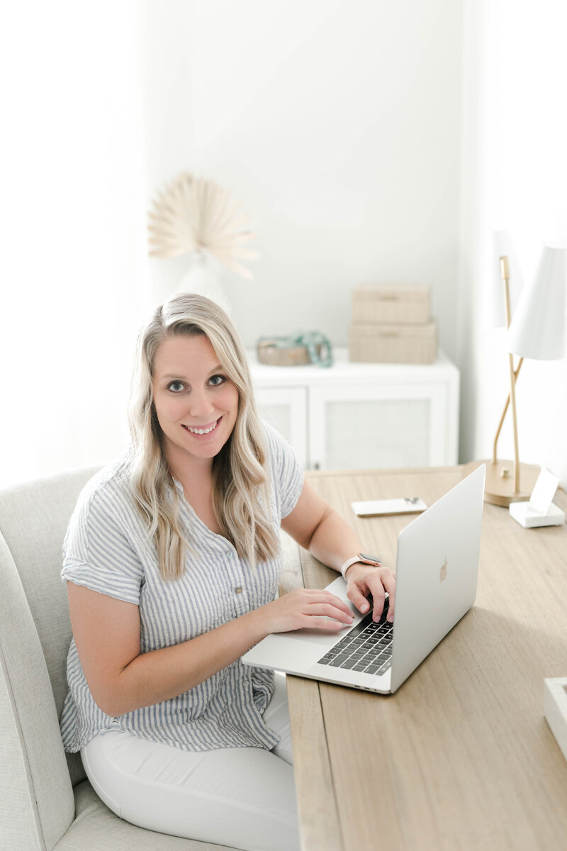 Kristin Wood Photography's operational business manager, Laura, smiles for portrait while working on her laptop at a desk