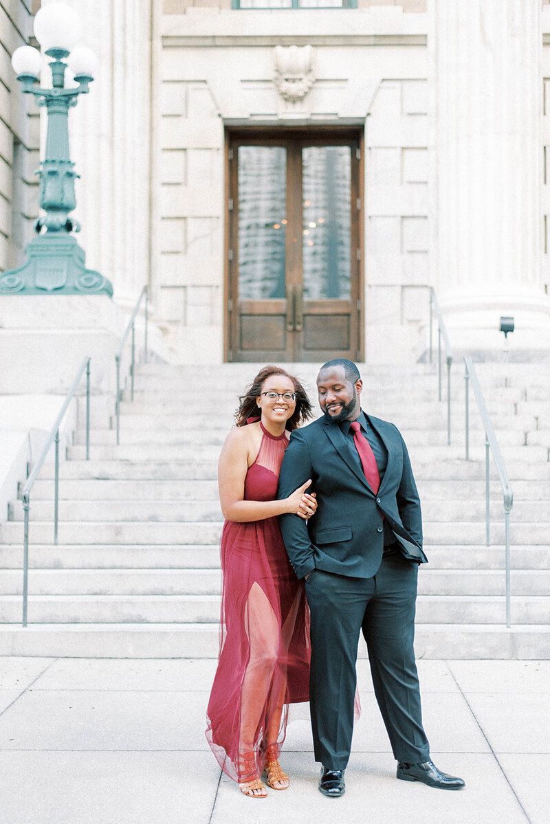 engagement session in St. Petersburg Florida with woman in a red gown holding onto her fiances arm as he is wearing a black suit with a red tie
