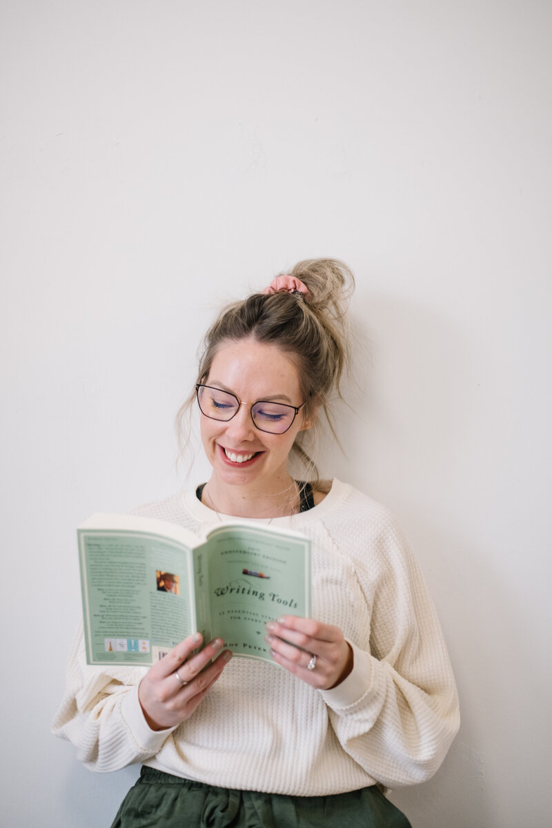 Sammy wearing glasses and a messy bun reading the Writing Tools book sitting in front of a white wall