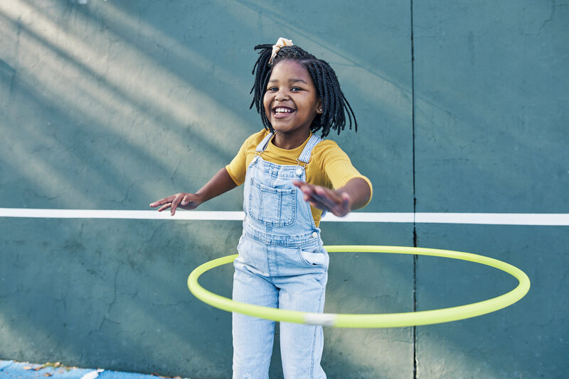 A young girl smiling while hula hooping outside on a sunny day
