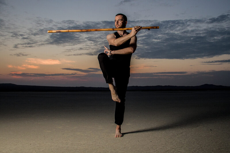 Branding Photography for Jason Campbell standing in desert at sunrise in yoga stance holding long wood flute