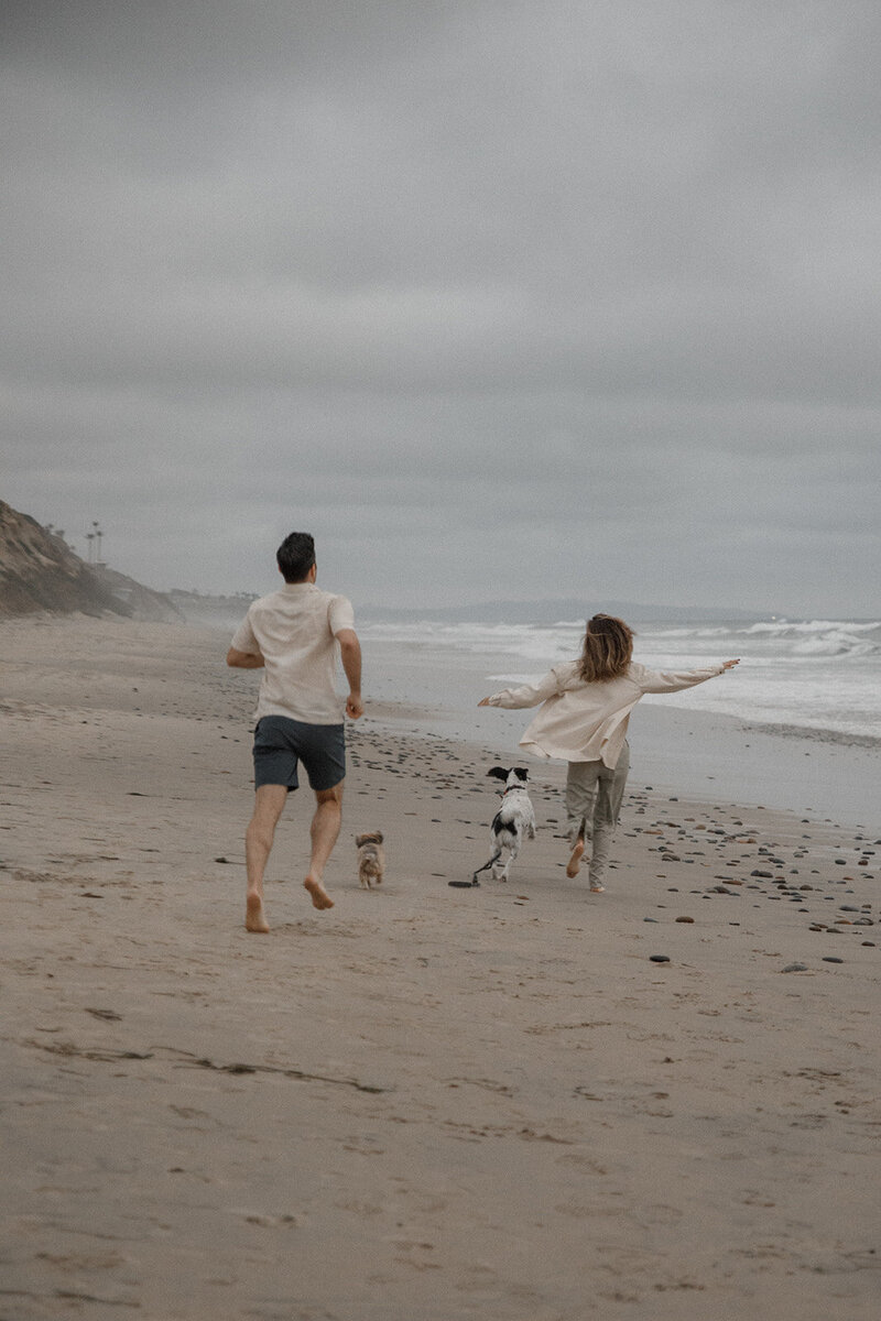 couple runs on the beach with dogs for engagement session in san diego