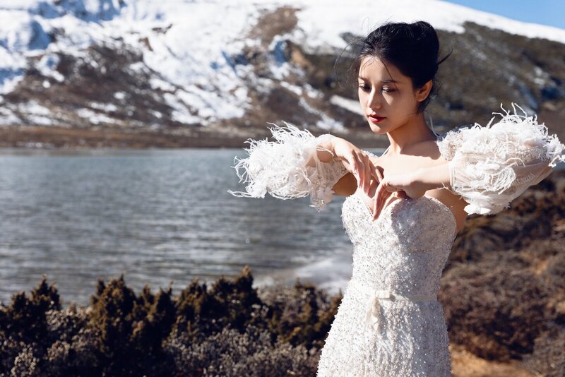 Dramatic shoot of a bride in a haute couture dress by an alpine lake in snow capped mountains.