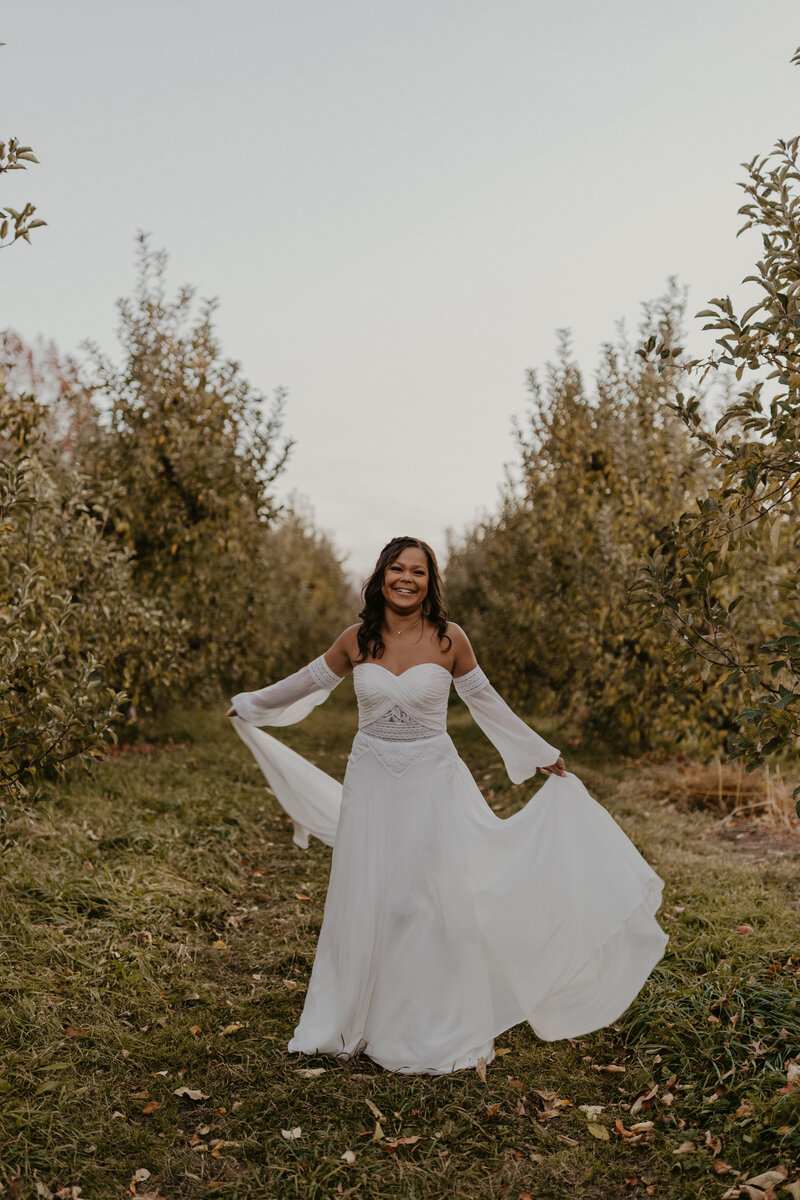Bride holding her skirt twirling in an orchard row at Robinette's Apple Haus and Winery.