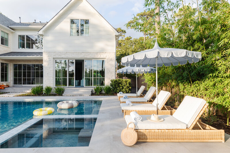 A white kitchen with white chairs and blue upholstered fabric around a white island styled with florals and fruit.