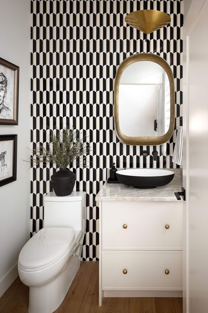 A powder room with a floor to ceiling black and white tile, quartzite counter and natural cream cabinets. 