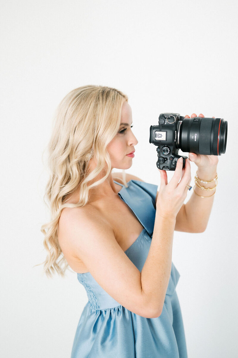 Blonde woman in blue satin dress holds camersa towards face