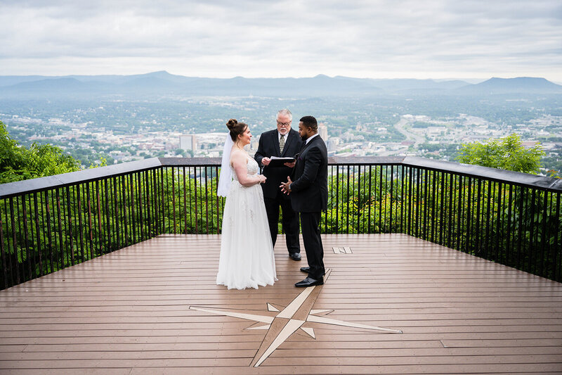 A couple begins their ceremony with their officiant at Mill Mountain with the Blue Ridge Mountains as their backdrop for their Roanoke, Virginia elopement wedding day.