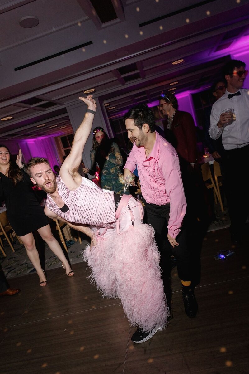 Gay man in pink vest with no shirt and feather chaps twerking on a man in a pink button down and black pants on the dance floor in the ballroom at the Line Hotel DC 