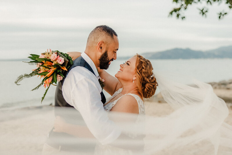 Bride and groom looking at each other with veil in foreground