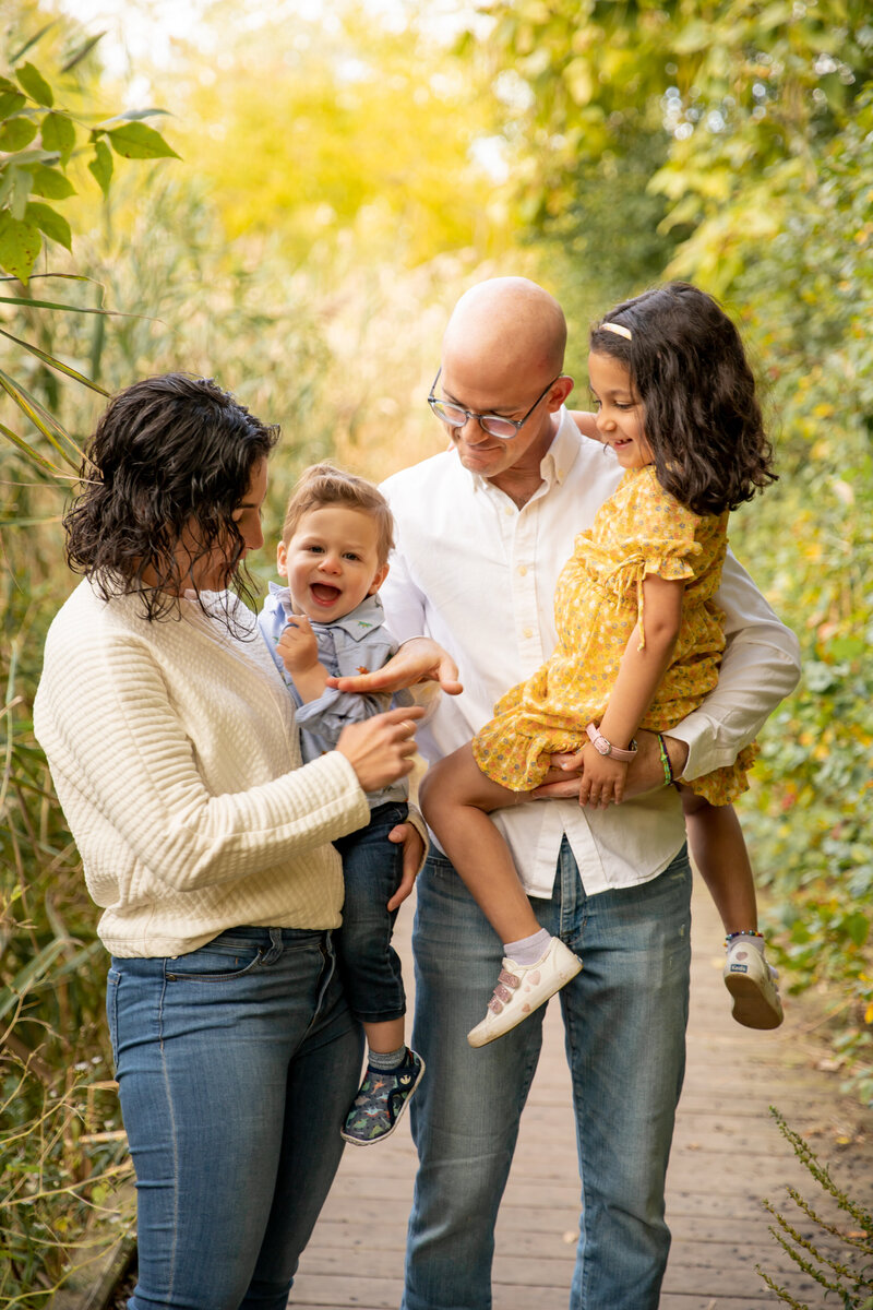 family with two young children stands on boardwalk during fall photo session at saginaw forest in ann arbor michigan