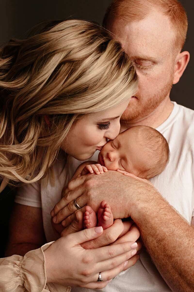 Man and woman kissing newborn in family portrait
