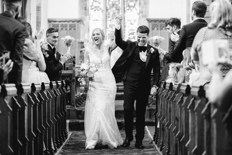 a bride and groom walking down the aisle with their hands in the air after their church wedding ceremony in lancashire