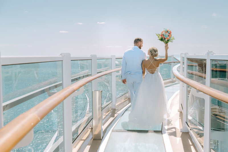 A couple cheers on the deck of their ship at their cruise wedding