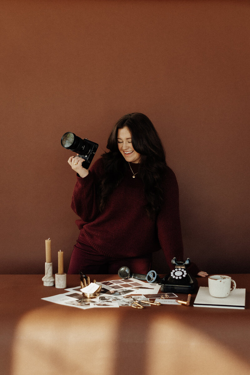 Elisabeth Eden at a table surrounded by moodboard pieces, holding her camera while planning a creative brand shoot, showcasing the process of visual storytelling and concept development.