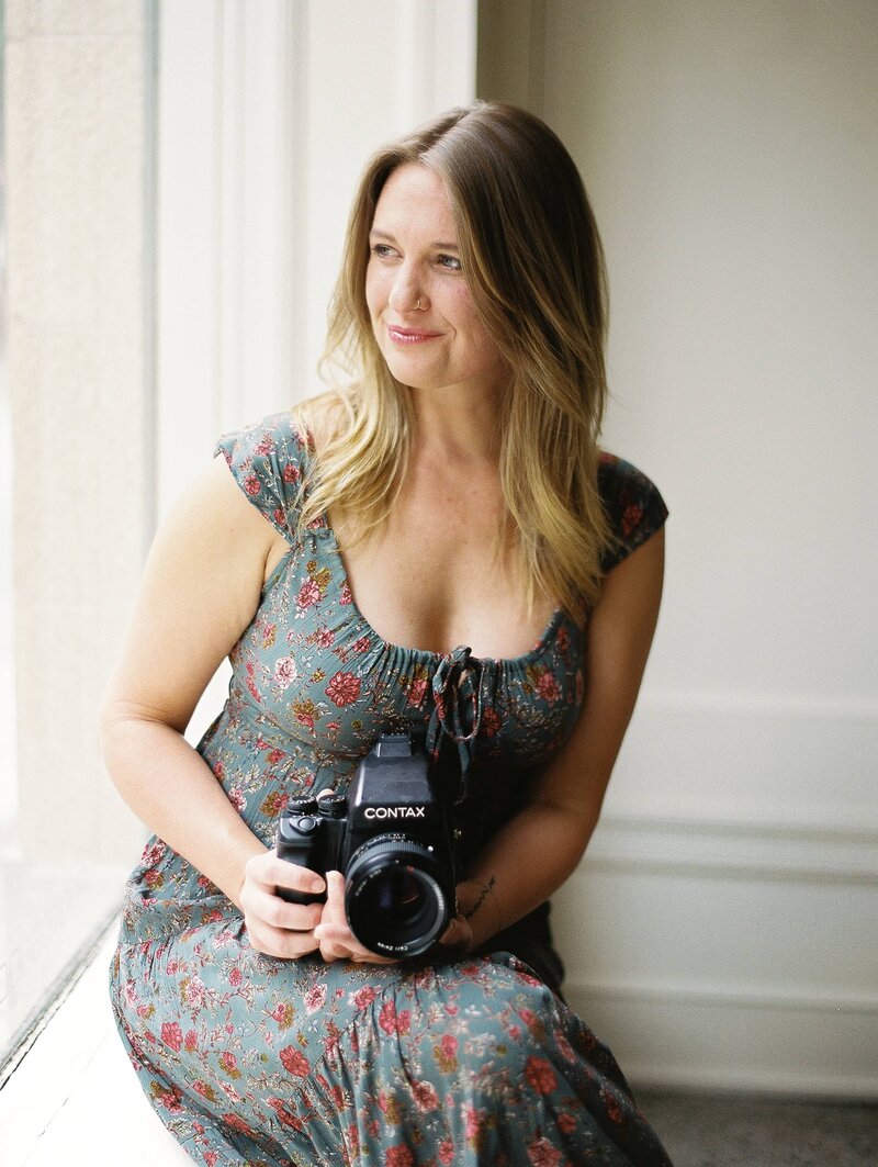 An Asheville wedding photographer poses next to a bright window with a film Contax camera in hand.