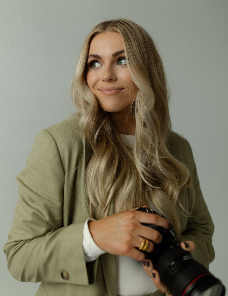Lifestyle portrait of Caitlyn Okerlund, Utah-based wedding and elopement photographer, seated and smiling with her camera.