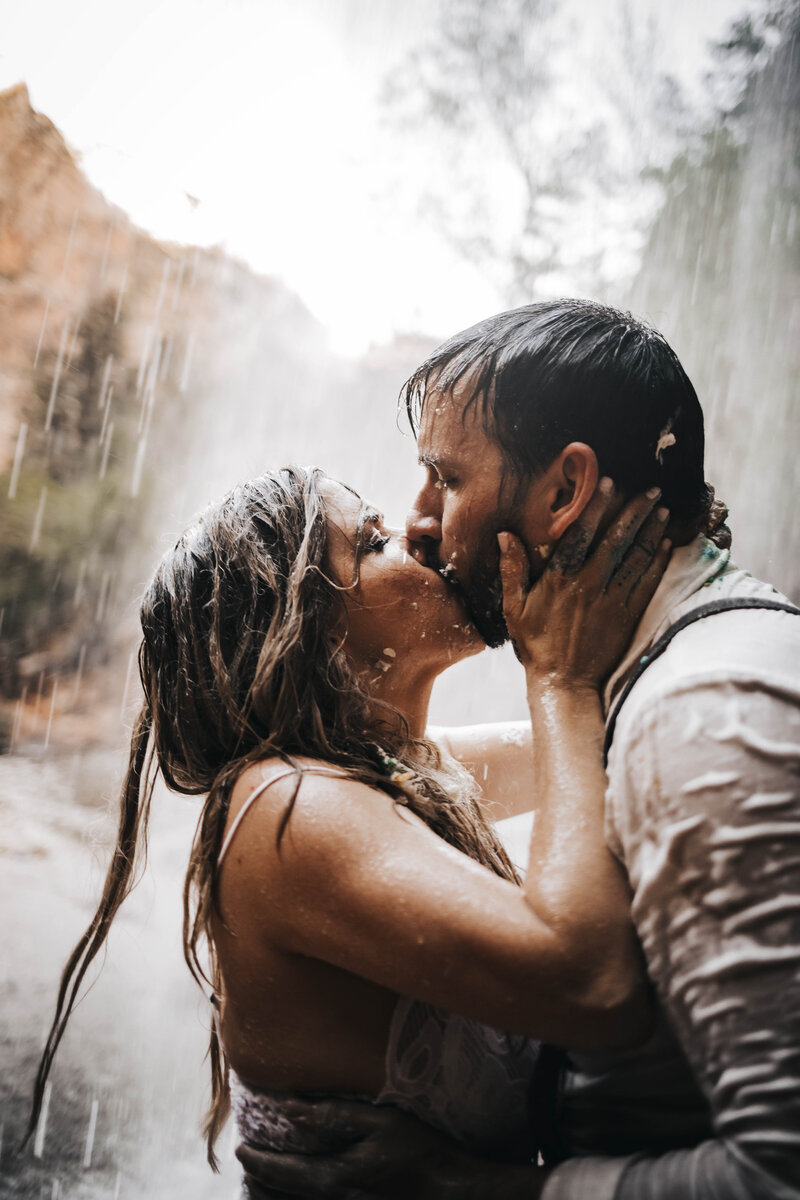 Couple kiss under a waterfall at Zion National Park covered in wedding cake.