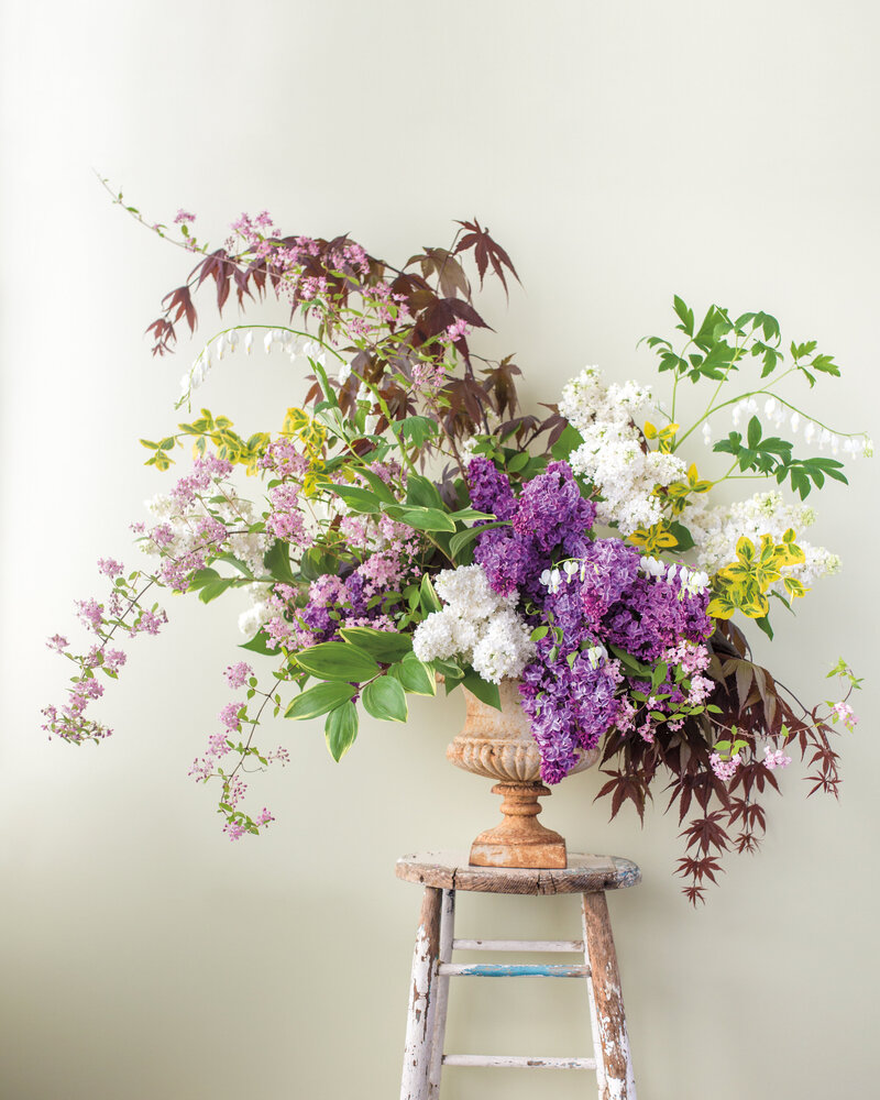 A colourful springtime arrangement of leaves and lilacs in a rustic urn captured in a Montreal studio. 