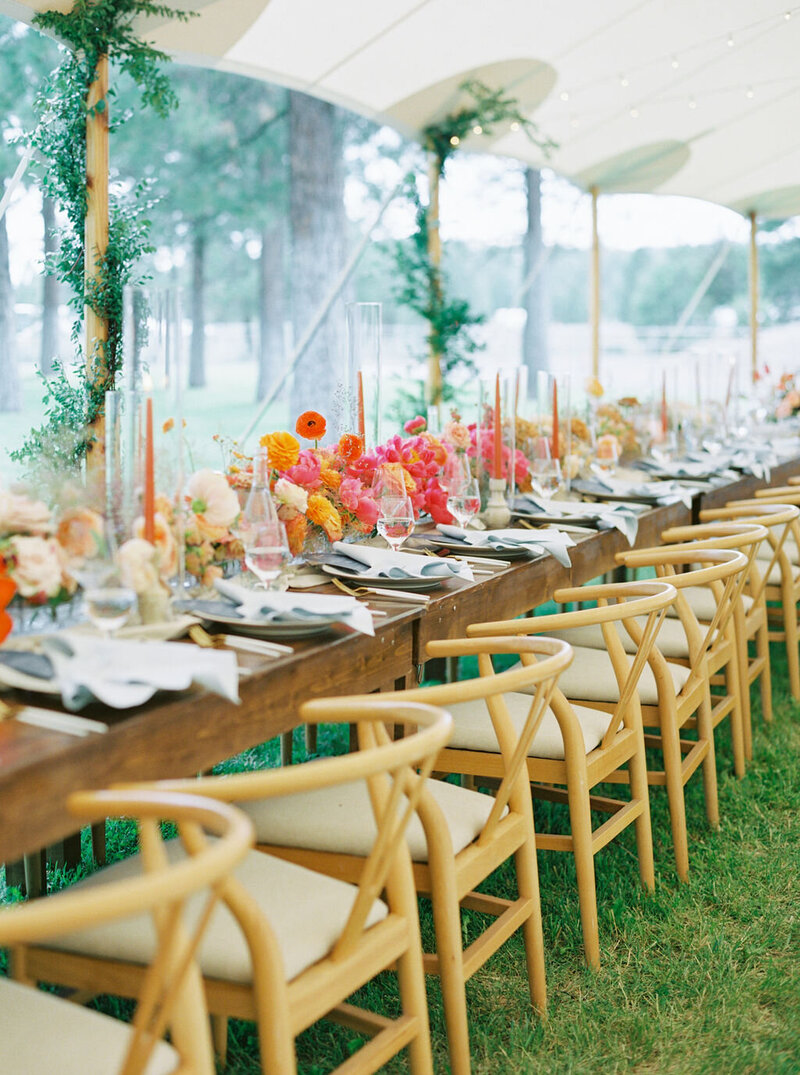Styled view of head table with ombré floral runner featuring peonies, ranunculus, and cosmos in blush to tangerine tones, under a sailcloth tent at Kelly and Joe’s wedding, by Summer Robbins Flowers in Bend, Oregon