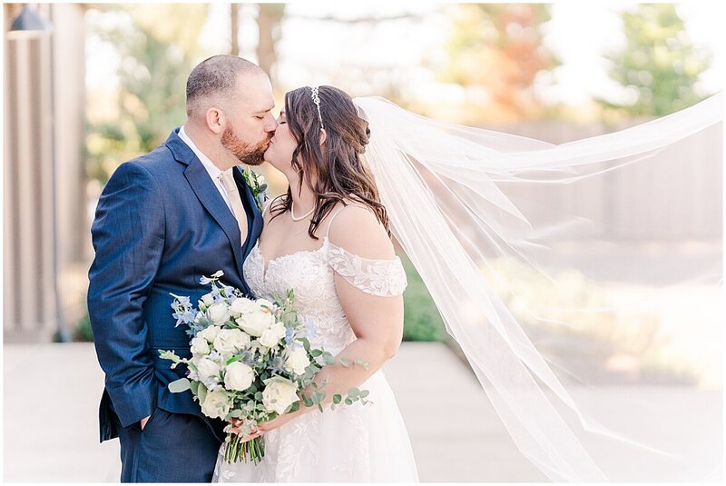 Bride and groom kissing wedding photo while veil blows in the wind at Abbey Road Farm 