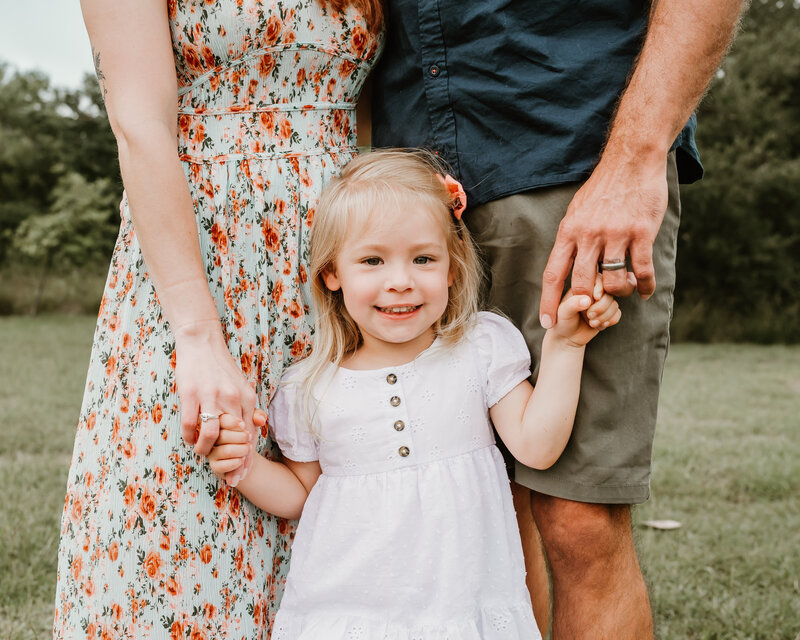 Little girl smiling while holding her parent's hands during a family photo session in Corpus Christi, Texas.