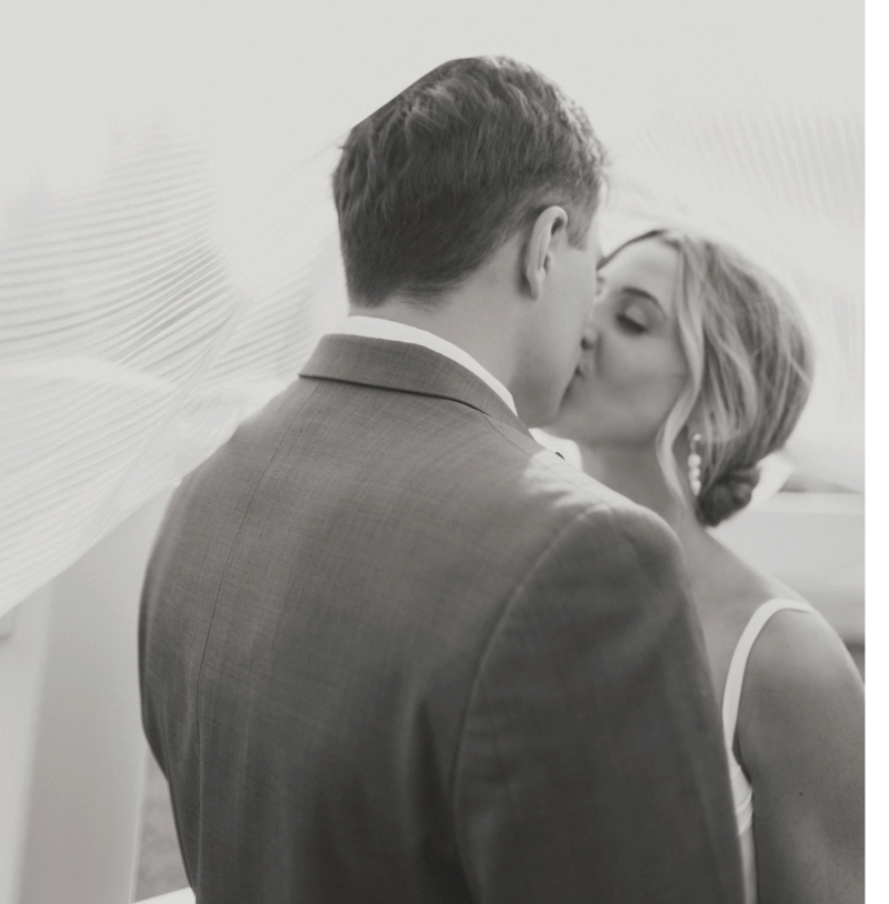 Bride kissing groom with her veil blowing in the wind