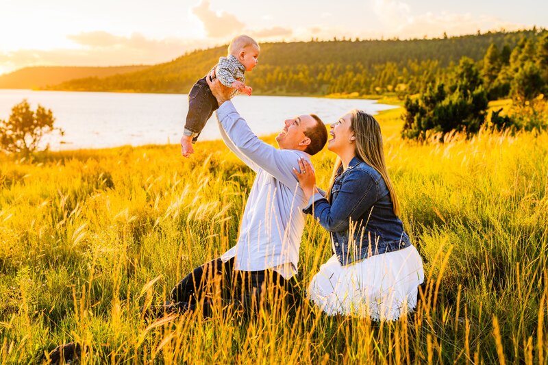 Family at Lake Mary Flagstaff holding young boy in the air smiling and laughing with golden hour sunset behind them