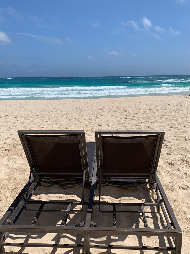 Two comfortable lounge chairs on a picturesque beach, showcasing a tranquil setting for destination wedding planning.