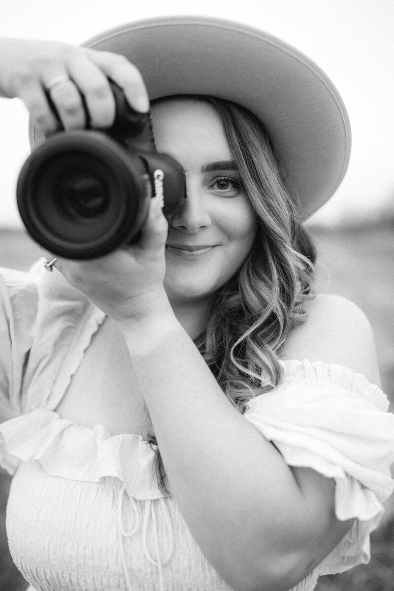 woman holding a camera up to her face while wearing a hat and looking at the camera