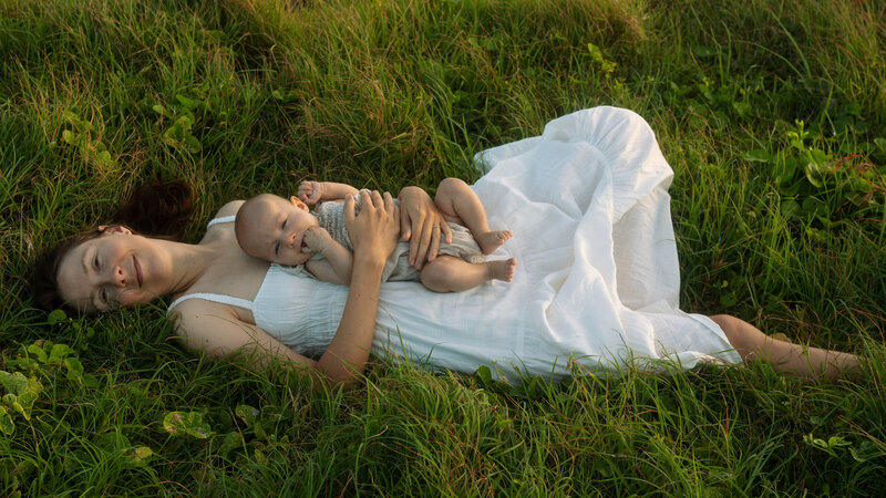 Mother and baby lying in lush grasses at Lennox heads, the mother is gazing at the camera holding her baby