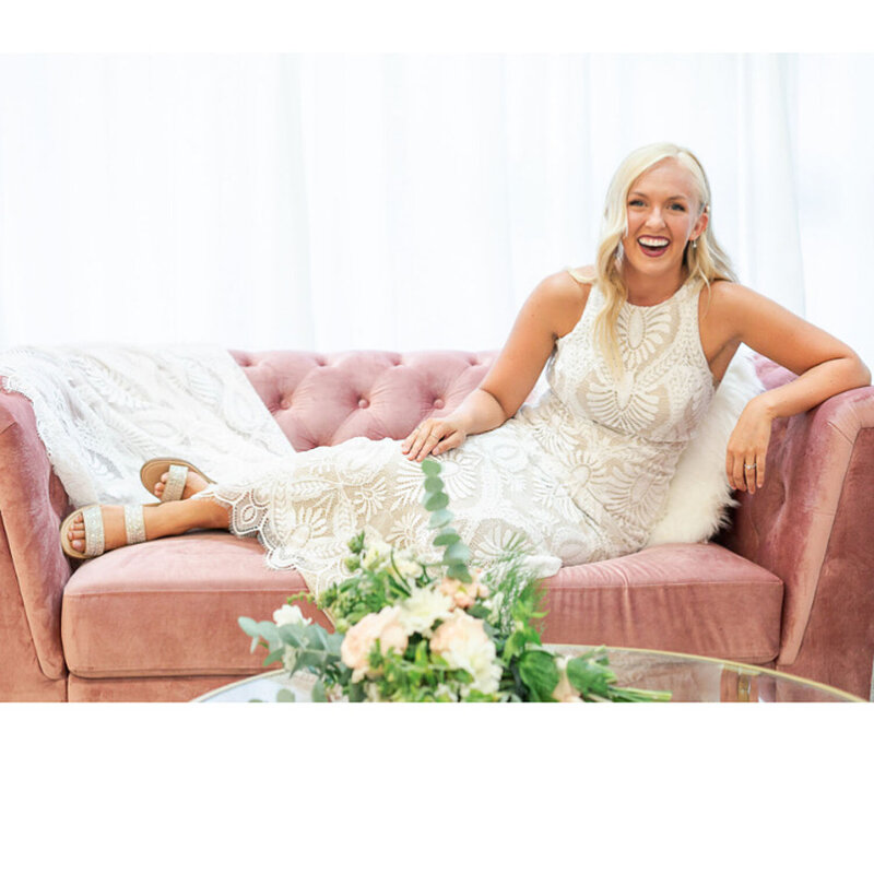 A bride lounging on a pink couch in a detailed lace gown