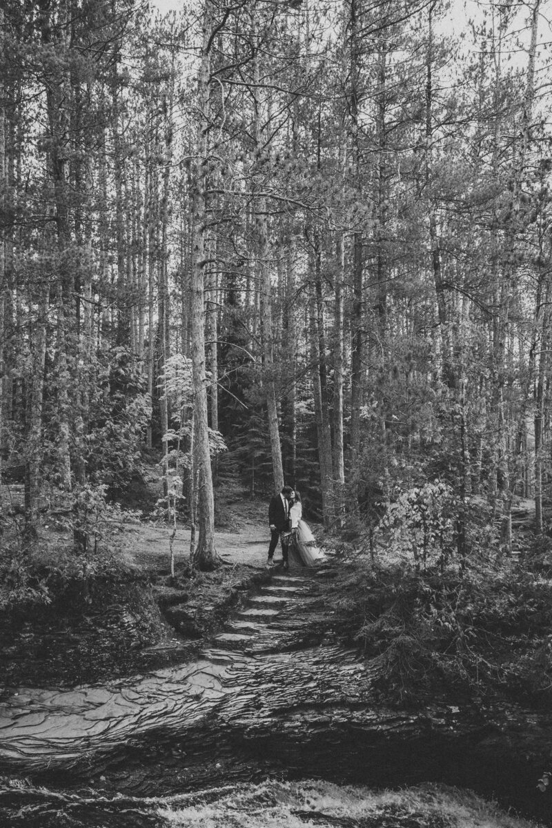 bridge and groom standing in the woods near steps when eloping in Bayfield, WI