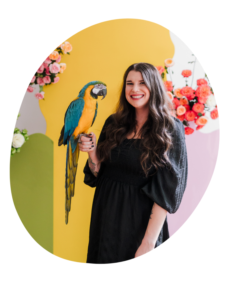 Taylor Doyle, the owner of The Floral Eclectic, standing in front of a backdrop she designed with her parrot.