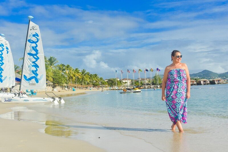 Woman in long colorful long dress walking on beach with palm trees and mountains in background in St. Lucia