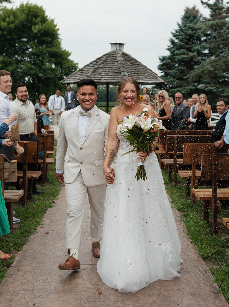 A warm summer wedding at Erickson Farmstead in Isanti, Minnesota. Gretchen and Abner walk down the aisle after saying "I do" and run through floral petals being tossed down the aisle.