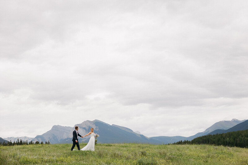 Couple walking through a field with the mountains in the background 