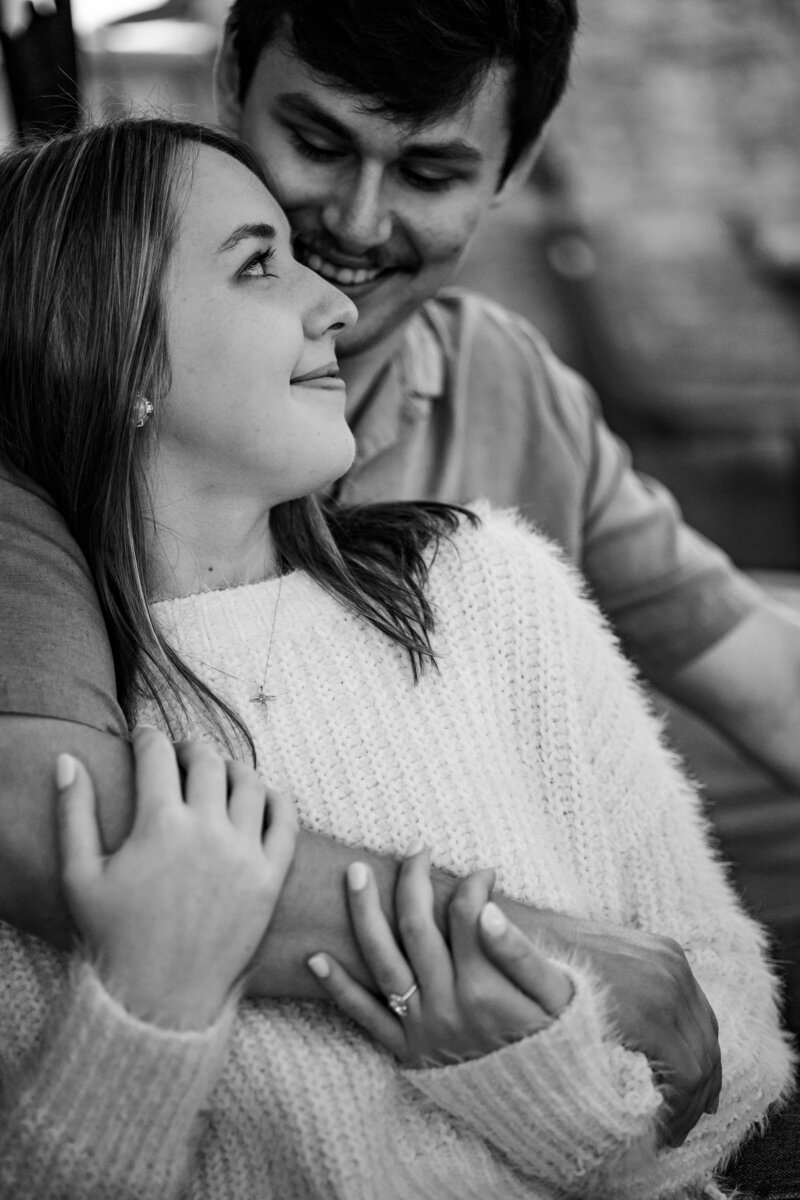 Black and white shot of Luke smiling at Megan while cuddling on the couch during their coffee shop engagement session in Memphis, Tennessee.