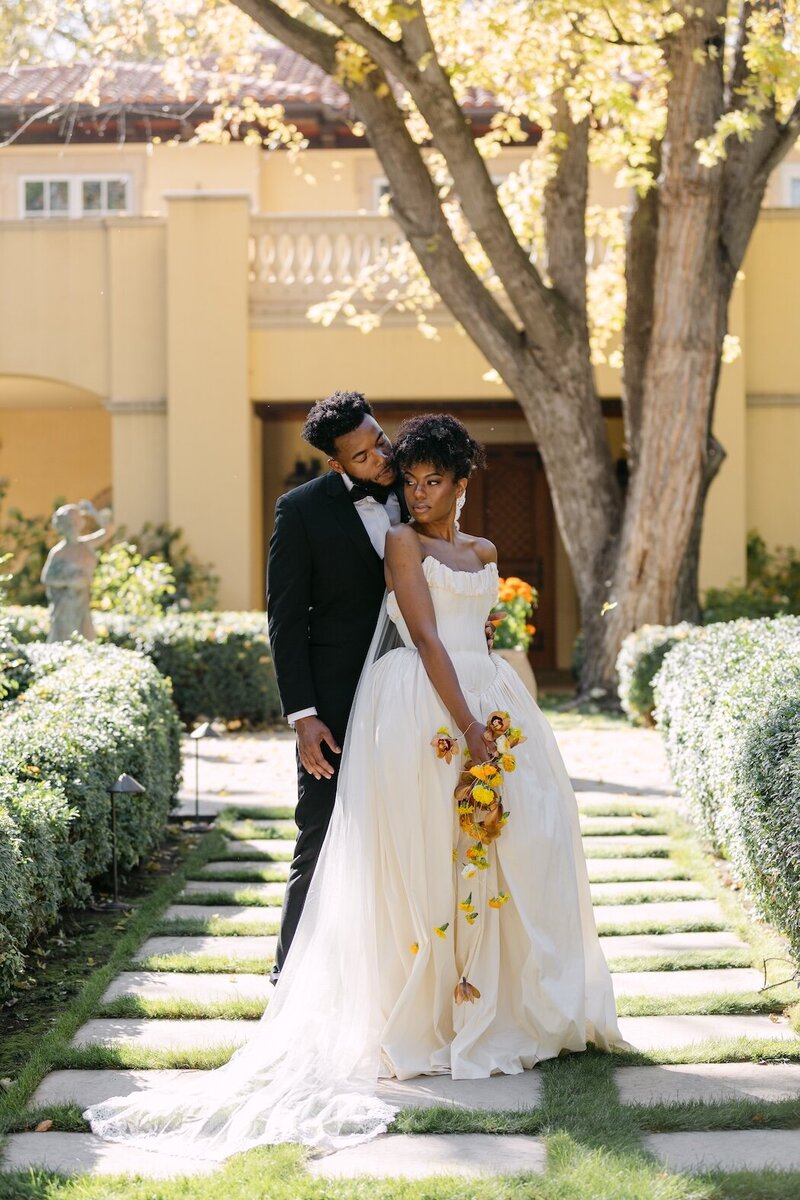 Bride and groom posing in a manicured garden walkway with yellow florals for their elegant Colorado wedding at Oceana's Gardens.