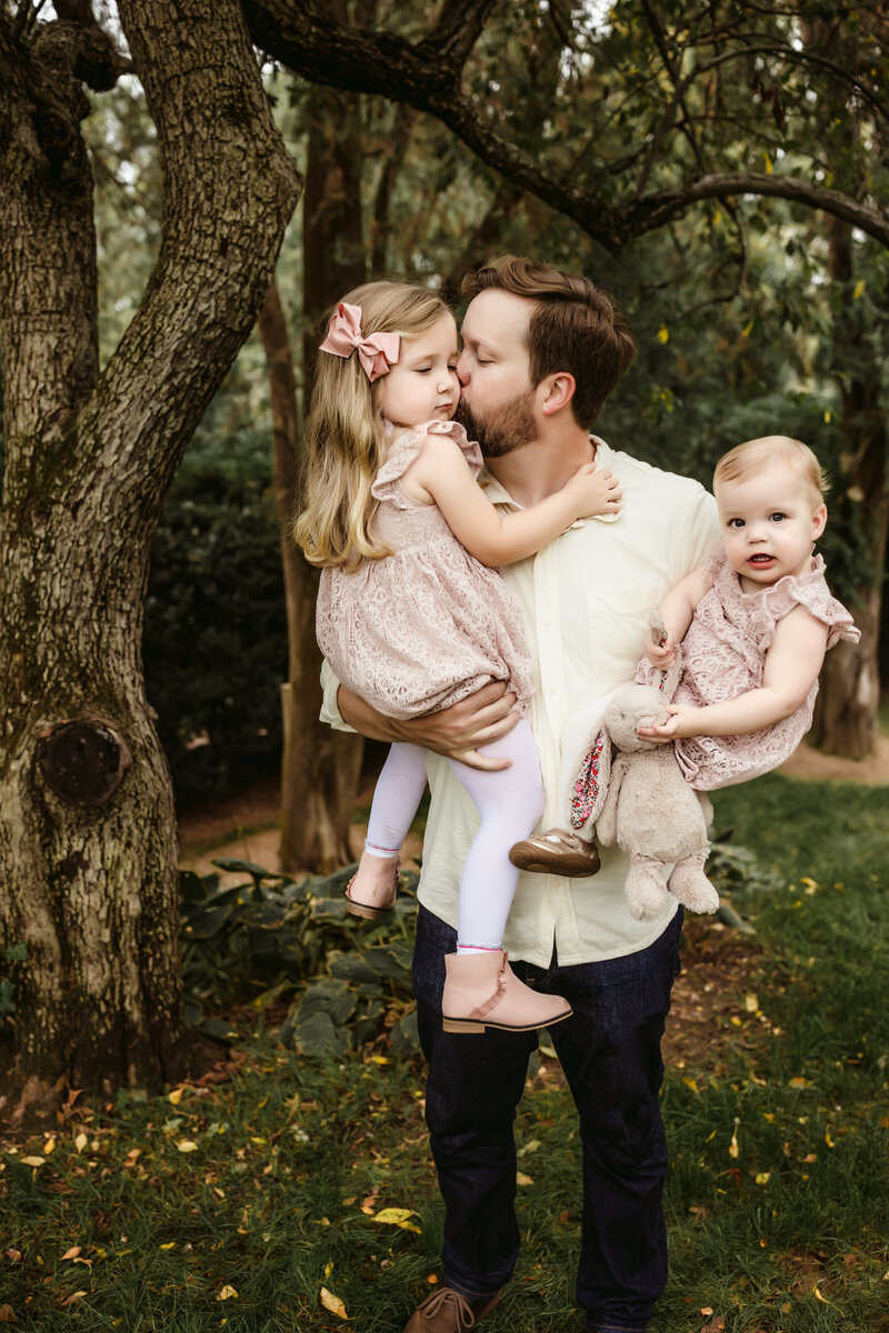 Dad kissing daughters cheek under magnolia tree in the garden