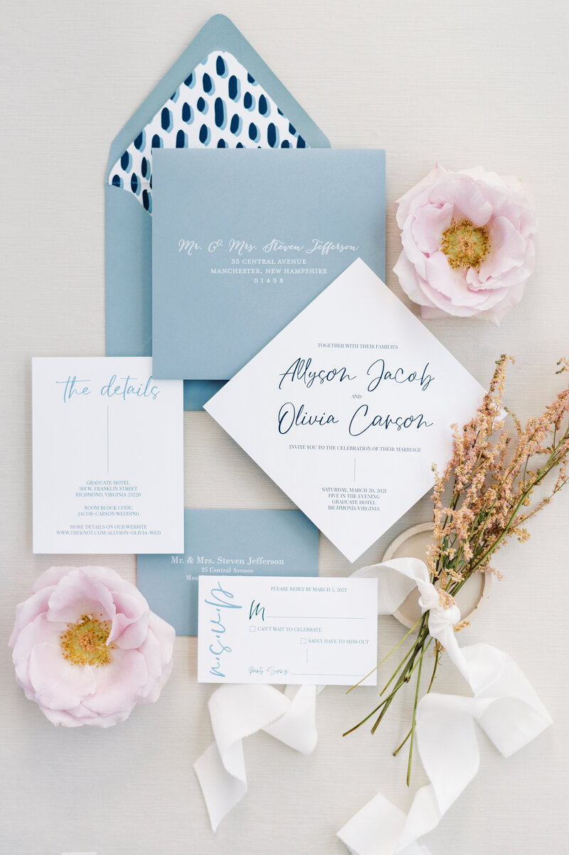 Dusty blue wedding invitation flatlay with pink flowers and ribbon.