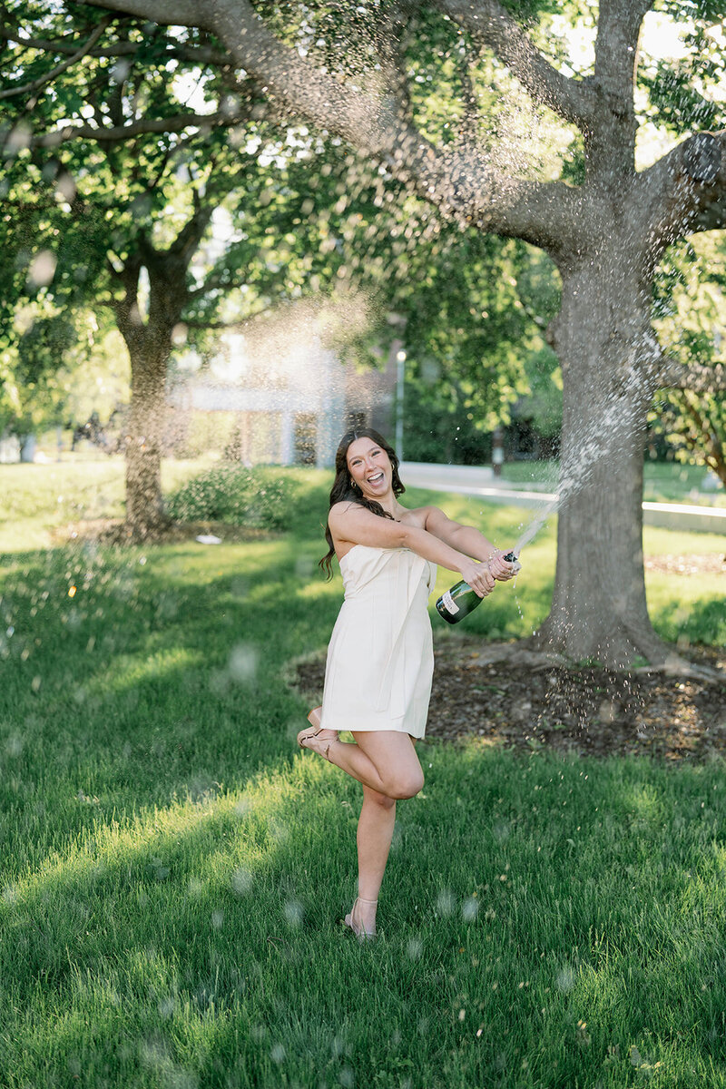 College senior spraying a bottle of champagne during her summer graduation session at Western Michigan University.