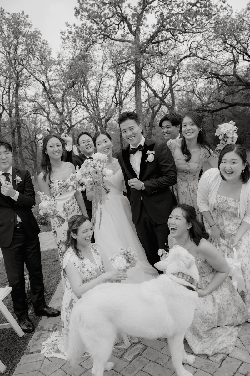 Black and white photo of bride and groom with wedding party smiling around them