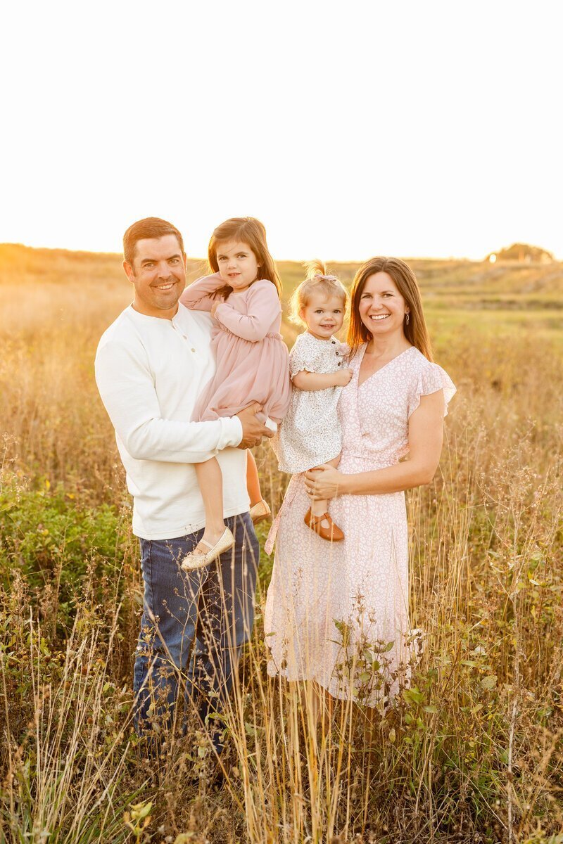 family smiling together in golden field, taken by wedding photographers in minneapolis