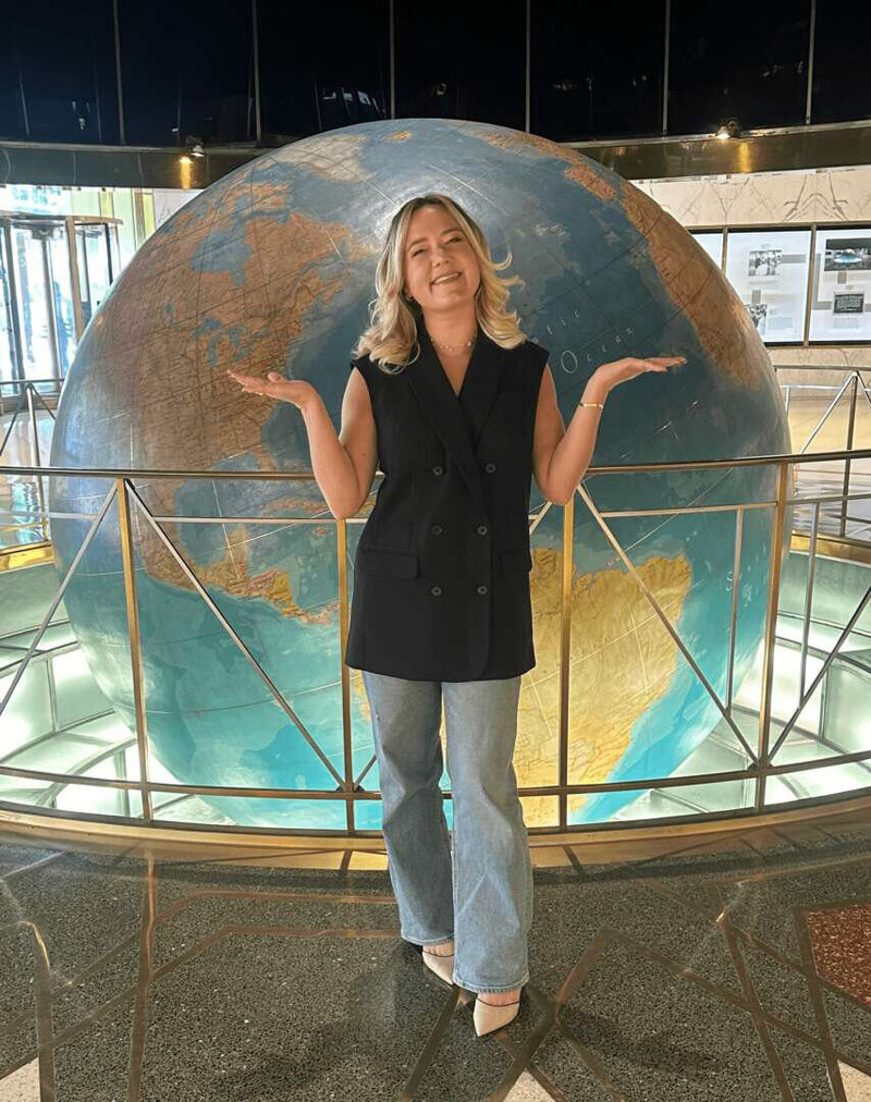 A woman stands confidently in front of a globe, symbolizing exploration and global awareness.